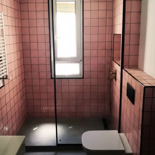 Mampara de vidrio con perfilería negra en baño rosa